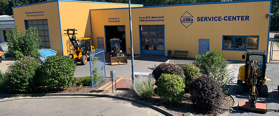 Das gelbe LöWa Service-Center in Görlitz mit beschrifteten Hallentoren für Stahlbau, KFZ-Werkstatt und Baumaschinen, davor Radlader und Bagger.